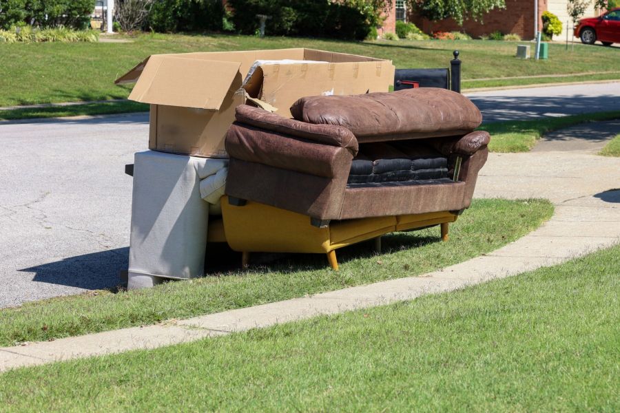 Discarded couch, mattress, and cardboard boxes piled at the curb in a suburban neighborhood for junk removal